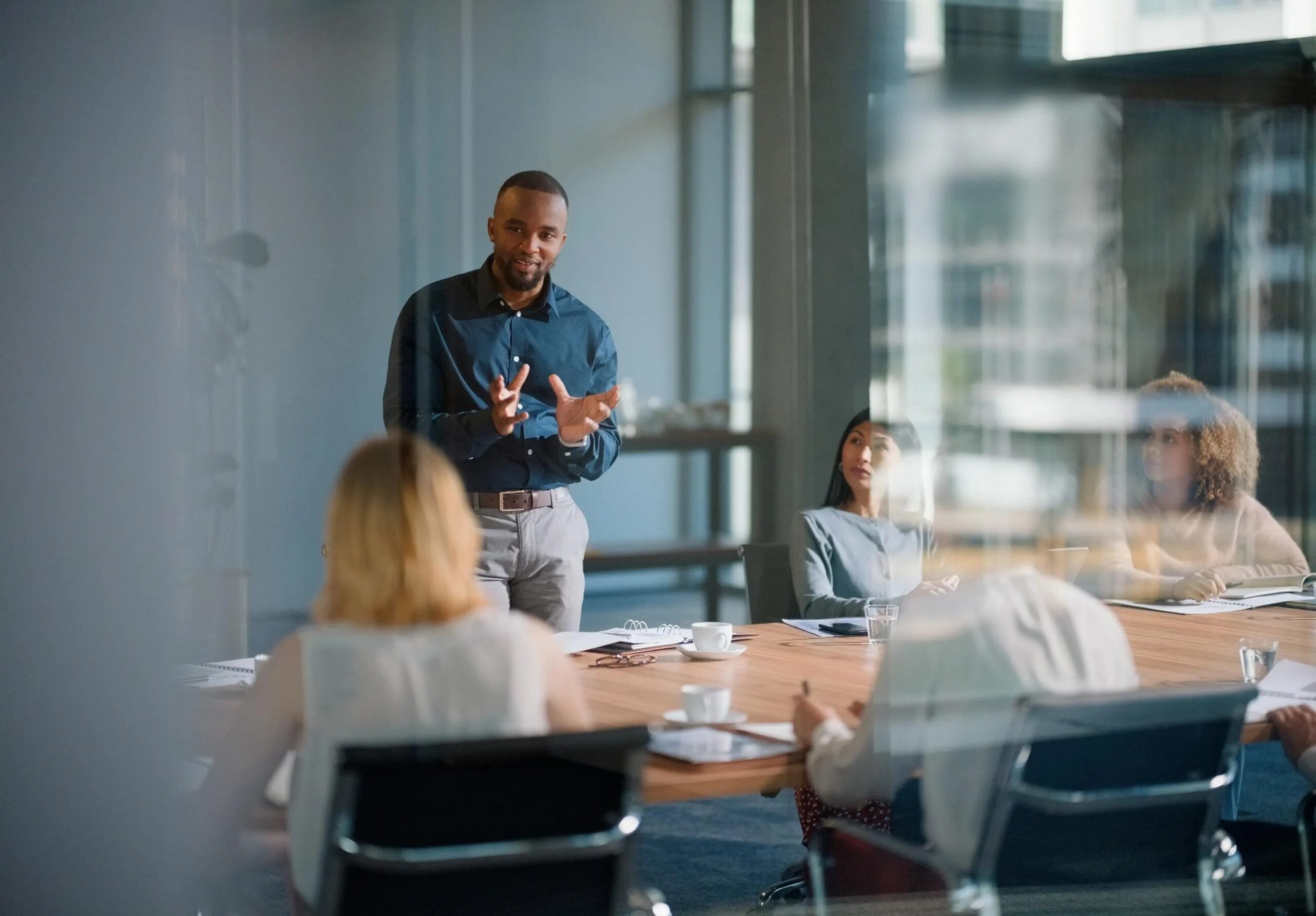 Executive presenting to colleagues through a glass office wall